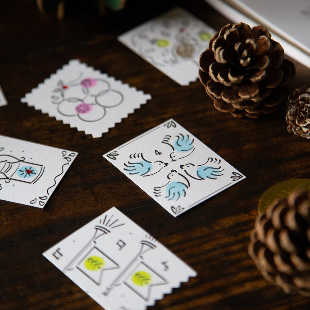 Colourful cards with hand-drawn designs on a wooden surface with pine cones.