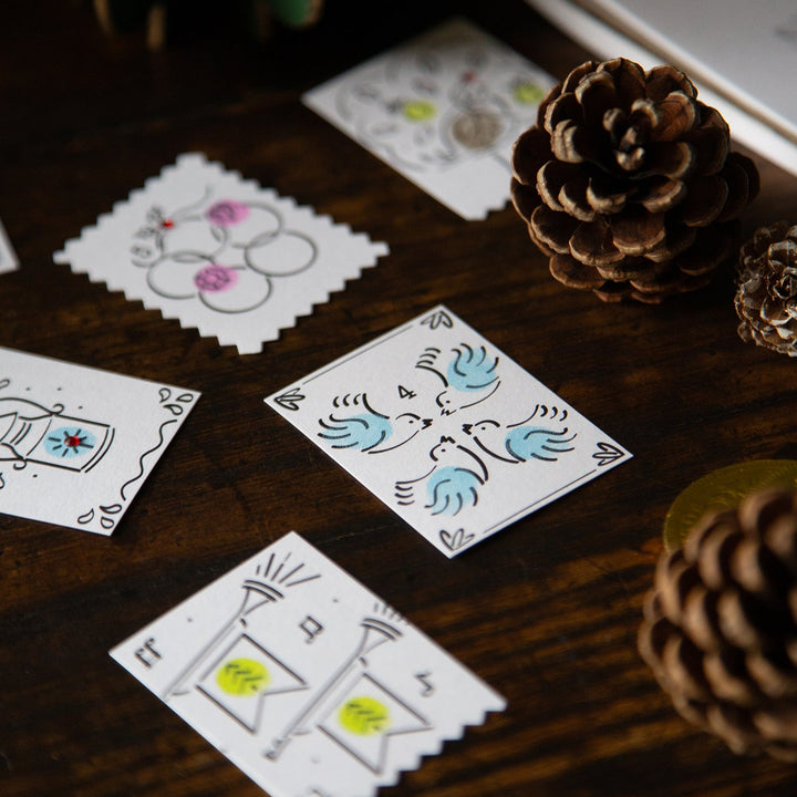 Colourful cards with hand-drawn designs on a wooden surface with pine cones.
