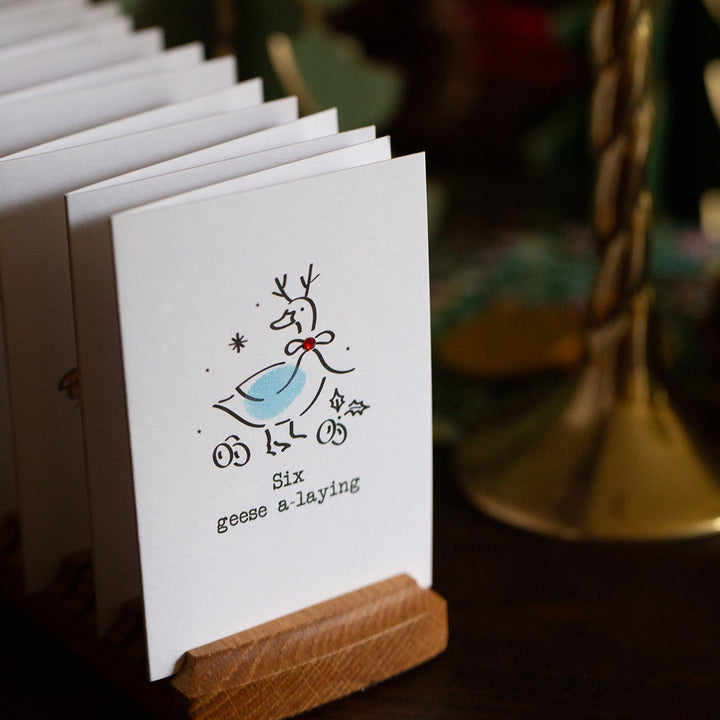 Row of greeting cards with a festive design on a wooden stand, blurred Christmas tree in the background.