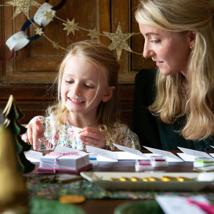 Woman and young girl sitting at a table with decorative string lights in the background