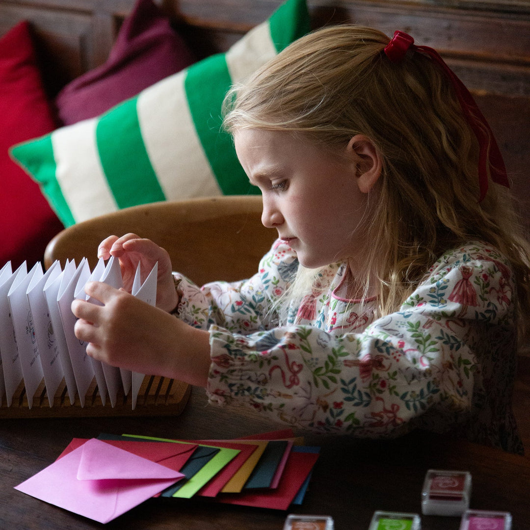 Young girl sitting at a table with colorful envelopes and stamps, surrounded by festive decorations.