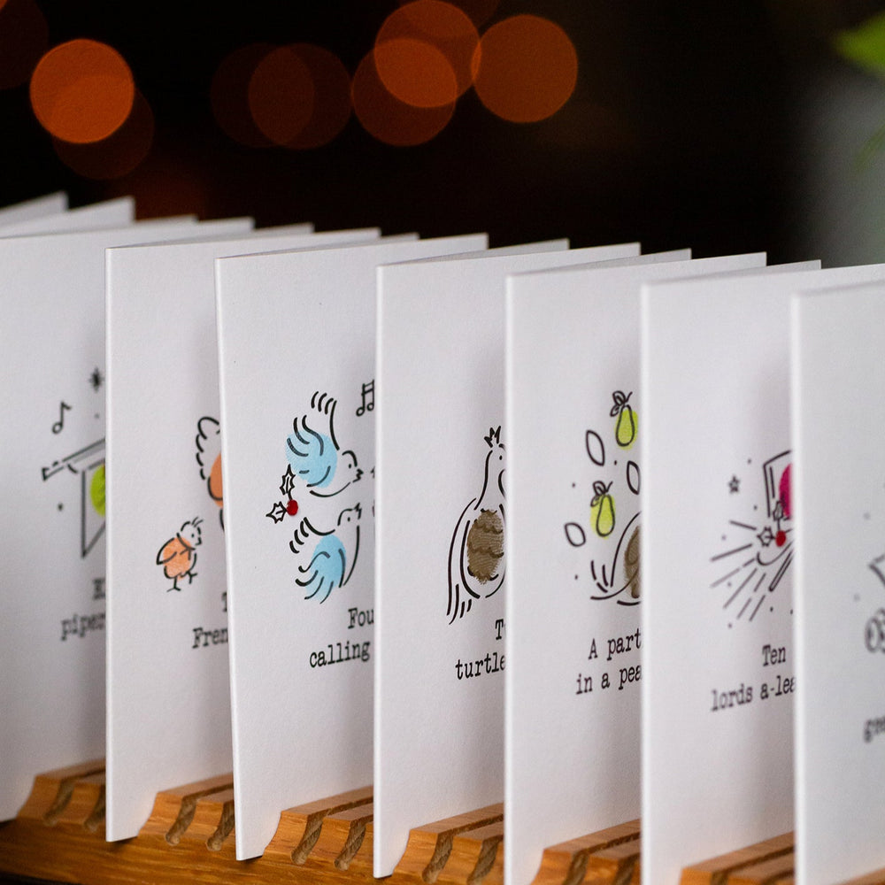 Row of small white cards with illustrations on a wooden stand against a dark background with bokeh lights.