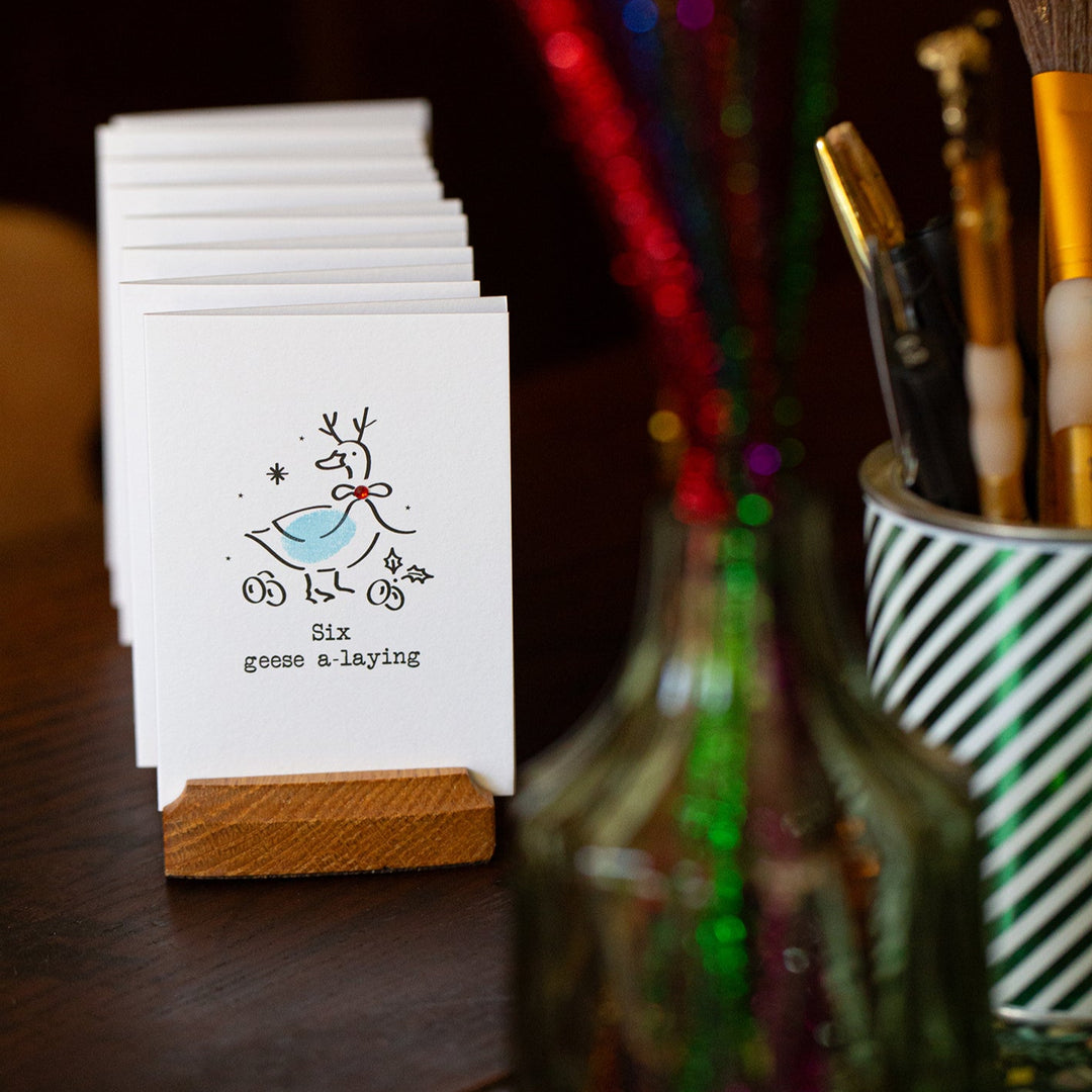 Stack of small Christmas cards with a goose illustration on a wooden surface with stationery items.