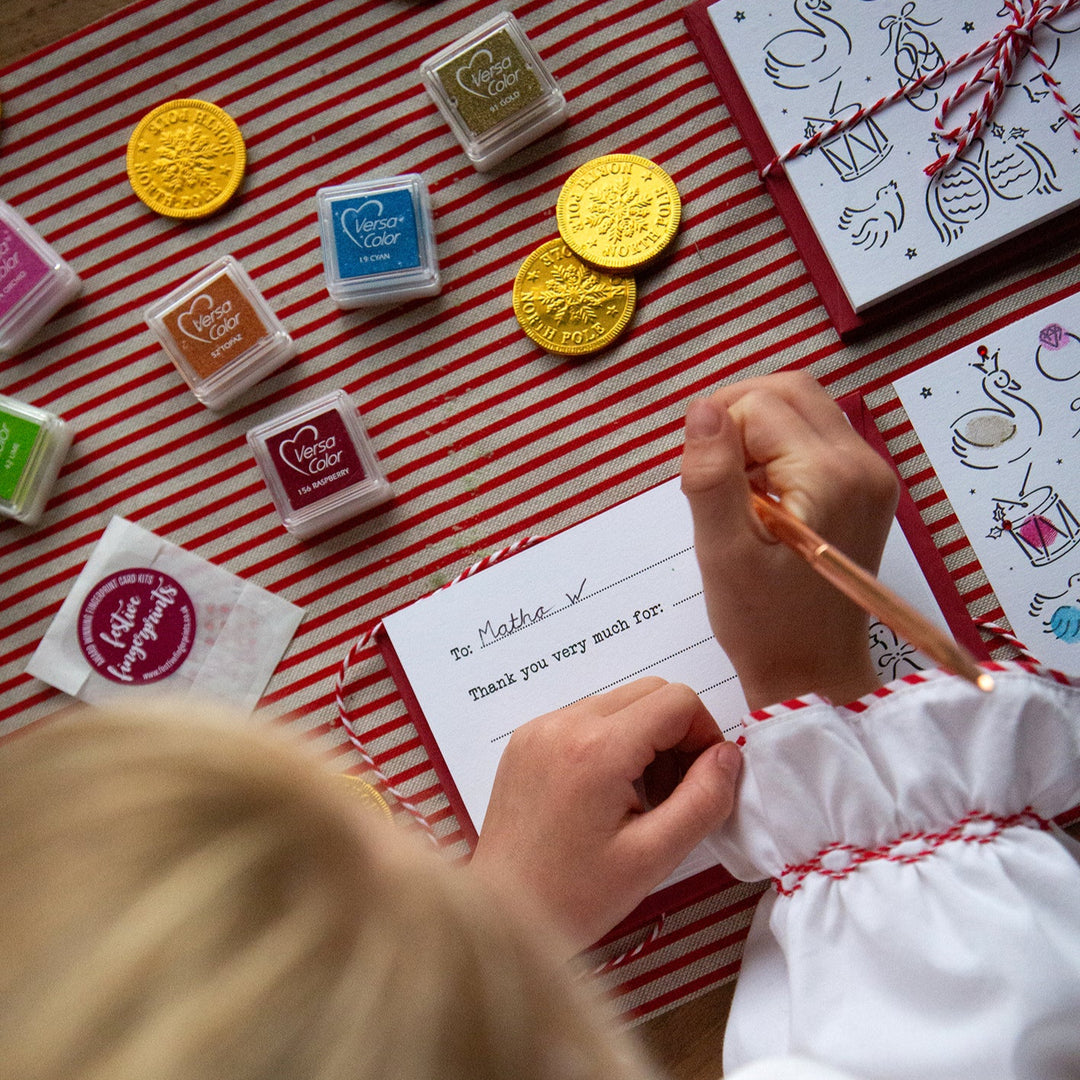Child writing a thank you card with colourful stamps on a red and white striped surface