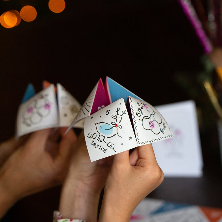 Hand holding a small paper fortune teller with blurred lights in the background