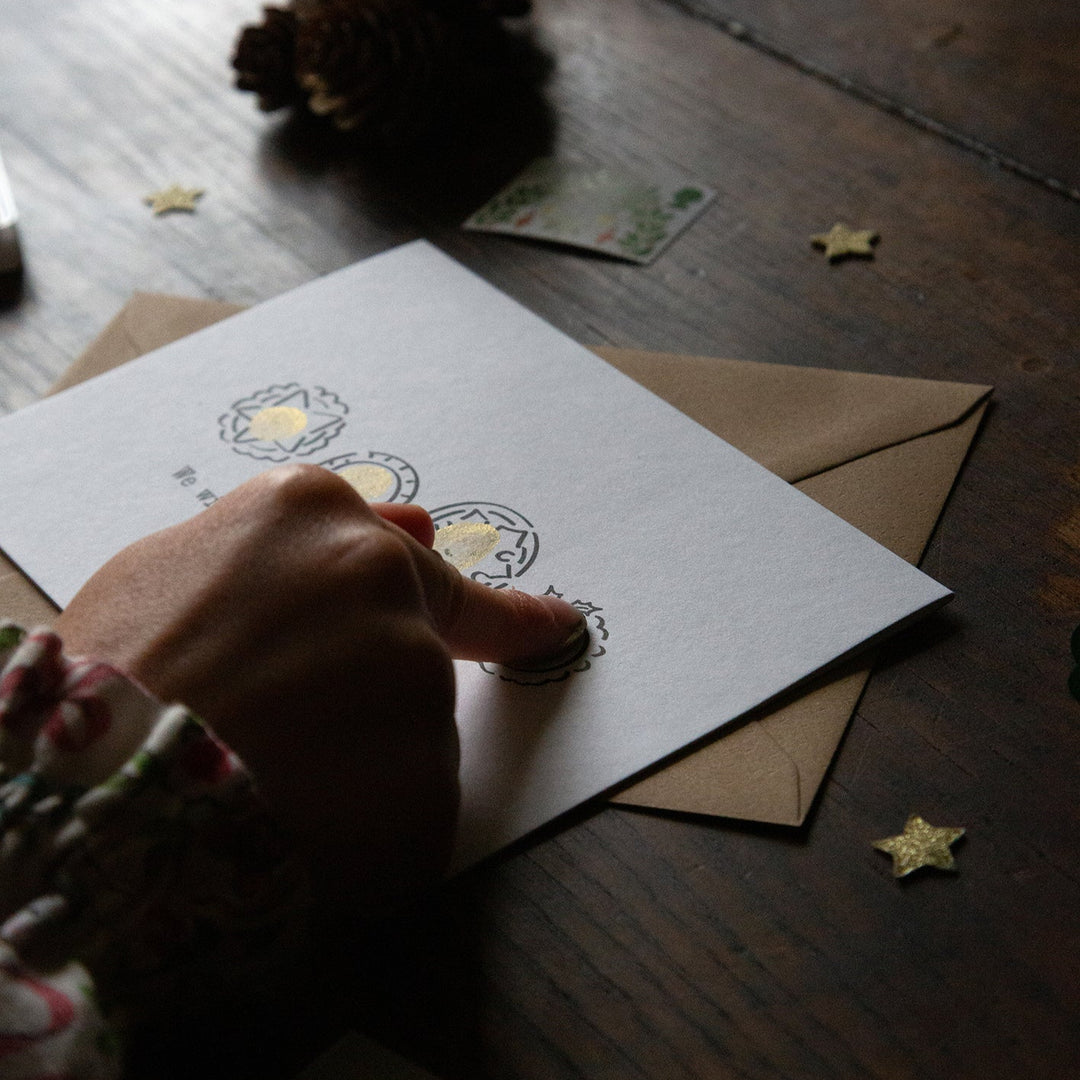 Hand stamping a card with a decorative design on a wooden surface.