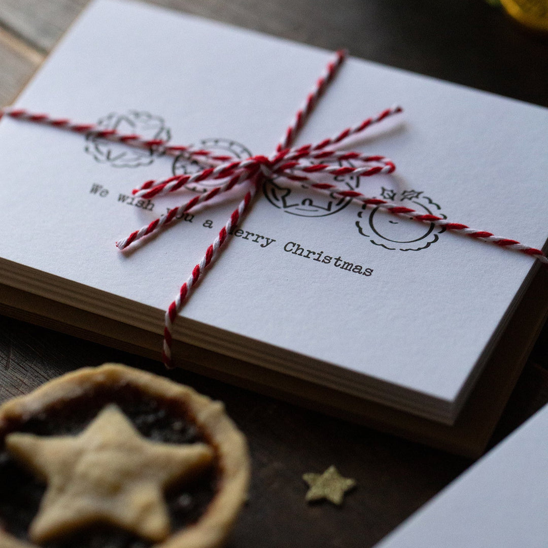 Stack of Christmas cards tied with red string on a wooden surface with a mince pie.