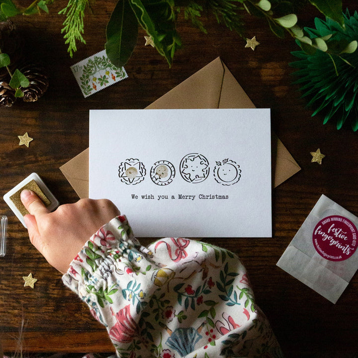 Child fingerprinting a Christmas card with ink pads on a wooden table.