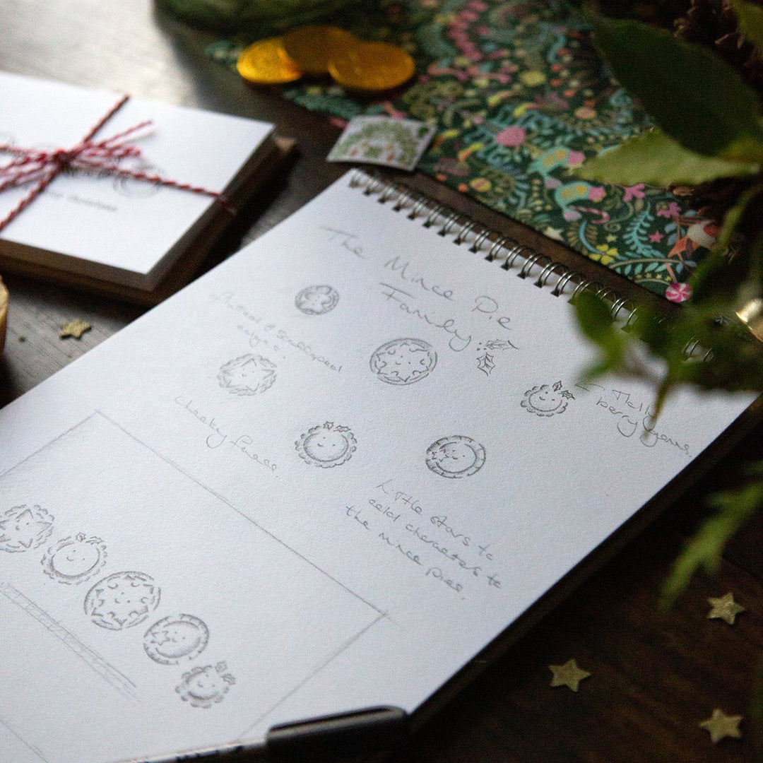 Notebook with design sketches on a wooden surface with decorative items.