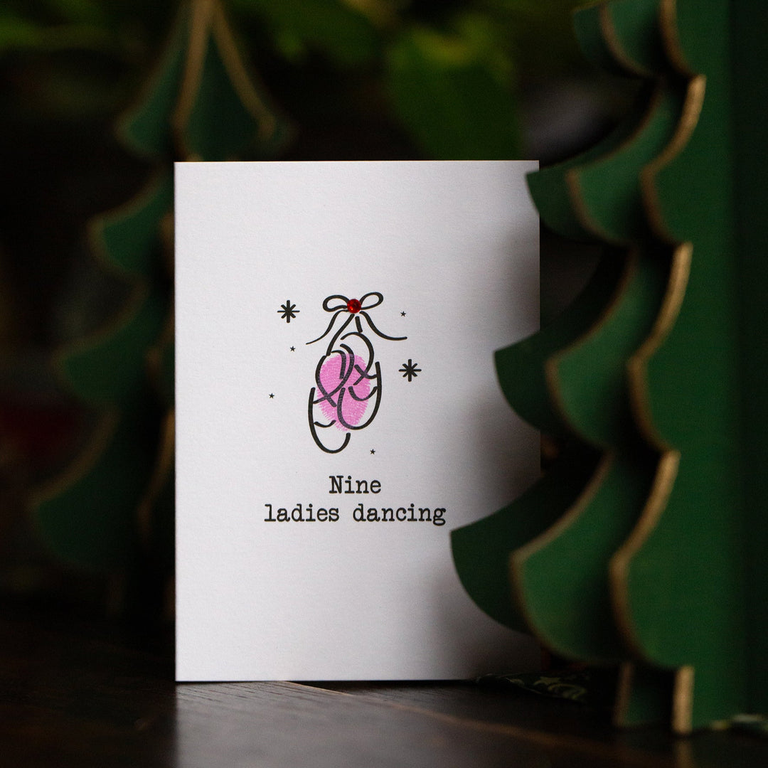 Card with a pink ballet slipper illustration and text 'Nine ladies dancing' on a dark background.