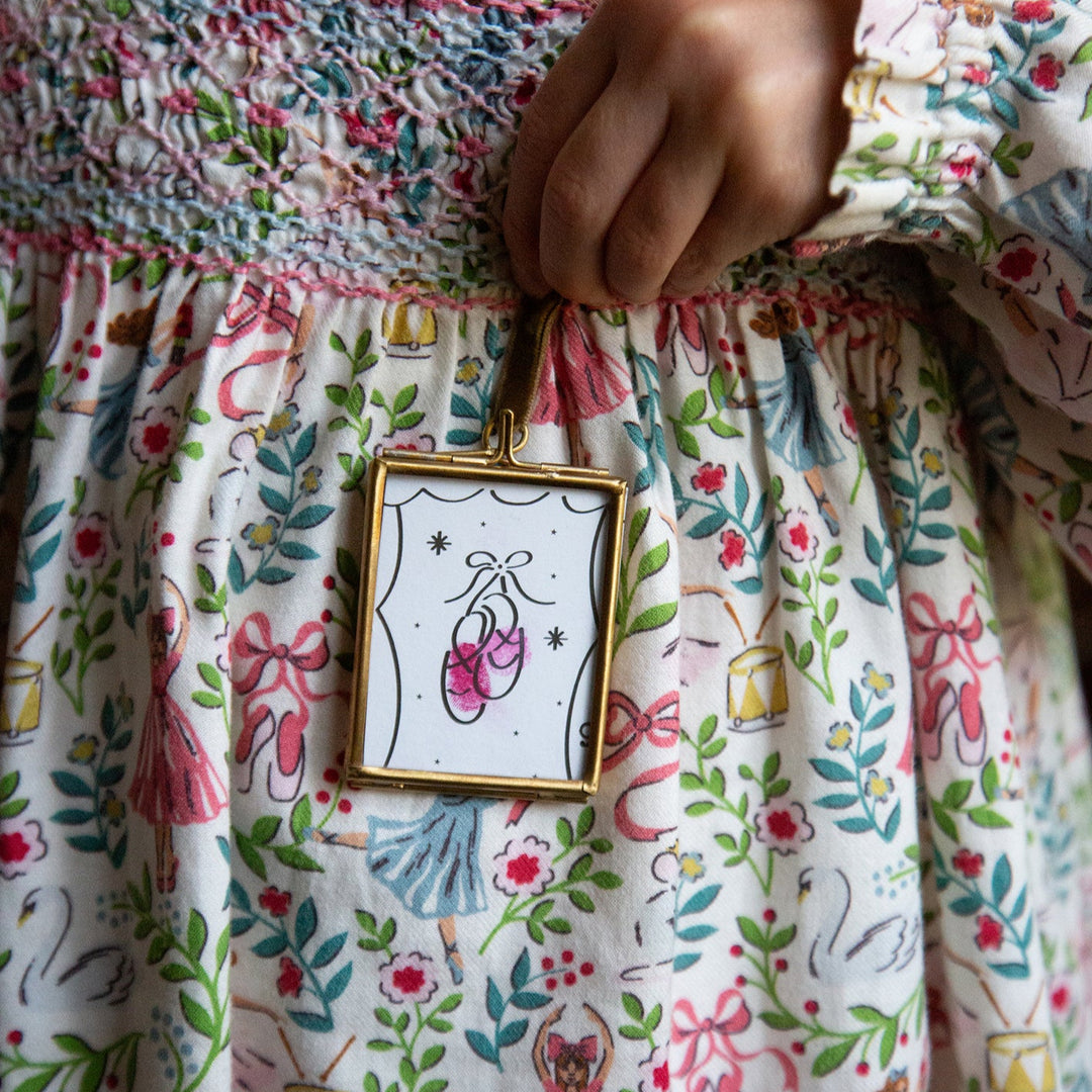 Close-up of a child's hand holding a small framed picture on a floral dress.