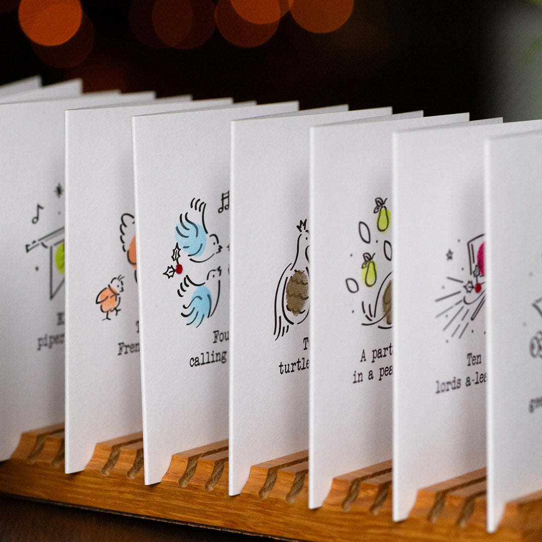 Row of small white cards with illustrations on a wooden stand against a dark background with bokeh lights.