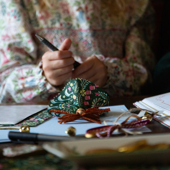 Child holding a pen with a decorated Christmas tree ornament on a table